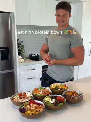A person, wearing a green shirt, standing in a kitchen with a series of bowls filled with various foods arranged in front of them on a white countertop.