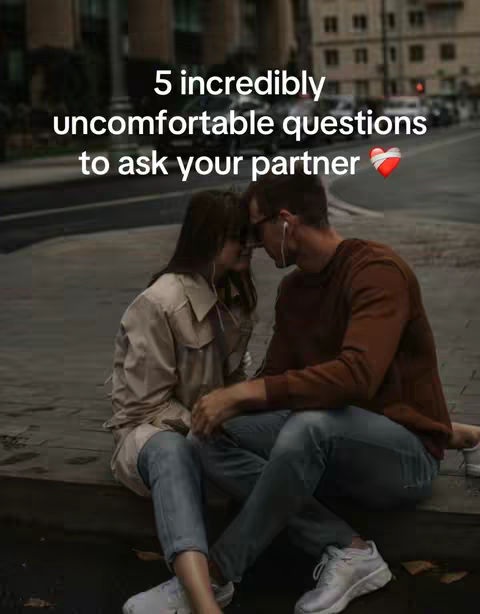 A couple is sitting close together on a ledge, leaning towards each other with their foreheads touching. They are wearing casual clothing, and there is text overlaid on the image that says, '5 incredibly uncomfortable questions to ask your partner' and a heart emoji.