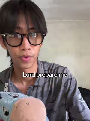 A young man with black hair and glasses is in the center, looking at the camera with an open mouth, likely speaking or singing. Text overlaid reads "Lord prepare me". A blue stuffed animal is partially visible in the foreground.