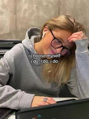 A young woman wearing glasses and a gray hoodie, her head resting on her hand. Text overlayed on the image reads: "i choose myself i do, i do, i do."