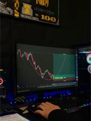 A person's hand using a mouse on a desk with a computer screen displaying a financial chart. The background includes a dollar bill art piece and a computer case with a fan.