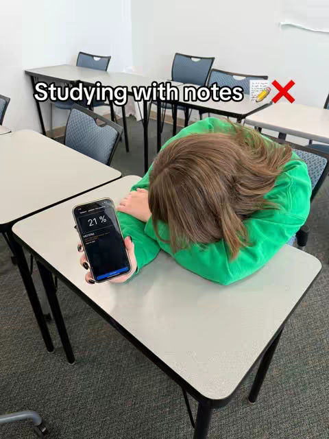 The cover image shows a person resting their head on a table with a smartphone in their hand inside a classroom setting. The person is wearing a green hoodie and their hair is visible. A smartphone with the screen displaying percentage is held in front.