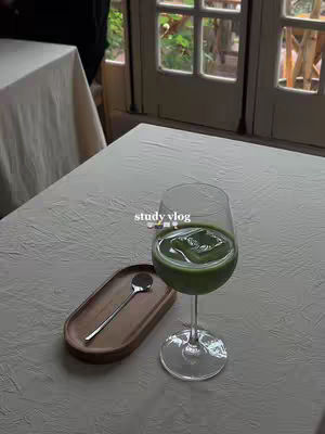 The cover image shows a table illuminated by natural light, with a glass of green beverage with ice on it, a wooden tray with a small spoon, and a view of a window in the background showing a cafe like setting. The image has soft tones.