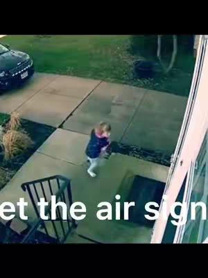 A surveillance-style video clip of a small child running forward on a concrete walkway in front of a house and car. Text overlayed on the bottom of the screen reads "meet the air sign."