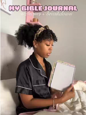 A young Black woman is seated in a bed, holding an open journal. The top text reads 'MY BIBLE JOURNAL', while a lower subtitle says 'step by step + breakdown'.
