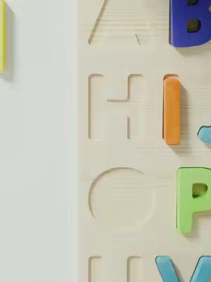 The image presents a close-up view of a wooden surface with cutout letters and colorful plastic inserts. The white background dominates the left side and a small portion of the top and bottom, leaving a visible border of light-colored wood where the alphabet is displayed. Cutout letters, including A, H, I, O, P, are visible in the wooden panel. The colors of the inserts vary. The lighting appears even and natural.