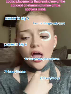 A selfie featuring a young woman with light skin and blonde hair, looking at the camera with a wide-eyed, slightly open-mouthed expression. The focus is on her face, and there are several overlaid text elements in different colors and positions, including references to astrological placements. She seems to be wearing minimal makeup.