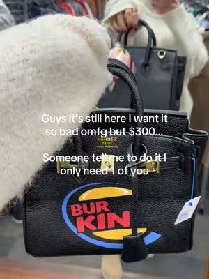 The image shows a close-up of a black Birkin-style handbag. The bag has a unique design with the words "BURKIN" in a logo style, suggesting a parody of the famous Hermes brand. Text overlays the bag, indicating the person wants to buy it. The bag is held by a person whose arm is visible.