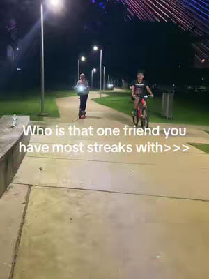 The cover image shows two people, one on a scooter and one on a bicycle, moving along a paved pathway at night. The scene has a slightly hazy quality with soft lighting from street lamps casting long shadows. The background shows dark green shrubbery with some illuminated architectural elements visible. The text overlay asks a question about 'streaks'.