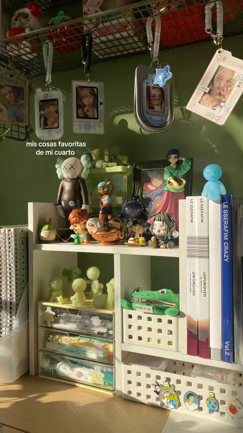 A well-lit, organized shelf in a room, filled with various decorative items. The setup includes a shelf with multiple levels, displaying figures, accessories, books, and keepsakes. Decorations include small figurines, framed photos, and hanging items. The color palette is soft, with a mix of white, green, and other pastel hues. The overall composition is neat and visually appealing.