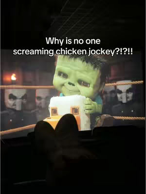A person seated in a theater watching a screen with a Minecraft-themed character and text overlayed. The viewer's legs are visible in the foreground.