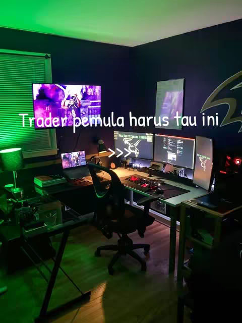 The image shows a desktop setup in a room with green and blue lighting. There are several monitors, a keyboard, and other computer accessories. Text overlayed on the image states, "Trader pemula harus tau ini."