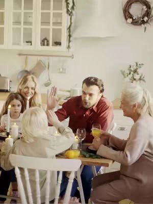 The cover image shows a family gathering. A man in a red shirt is gesturing with his hand across the table. The table is set with glasses and food. Other family members are a blond woman, a girl holding a candle and an older woman