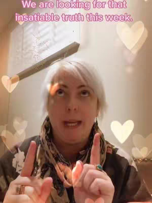 The image shows a woman with short white hair looking upwards and speaking. She's wearing a scarf and top. Behind her are blurred-out heart shapes. In the background, a pencil with an eraser is seen angled to the upper left, and text is overlaid at the top.