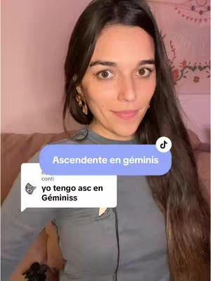 A woman with long brown hair is centered in the frame, smiling slightly. Behind her is a blurred background, likely a room interior. A blue oval with white text that says "Ascendente en géminis" is floating above her. A TikTok comment is shown with the text "yo tengo asc en Géminisss".