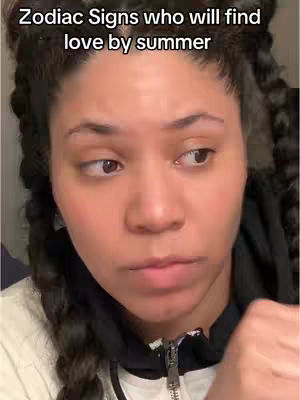 A close-up shot of a woman with dark hair styled in braids, looking slightly off-camera with a contemplative expression. Text overlayed at the top says "Zodiac Signs who will find love by summer". The woman is wearing a white top and a black zip-up jacket.