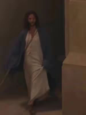The cover image features a person, possibly Jesus, walking toward the viewer. The person is dressed in a white robe and a blue shawl, with long, dark hair and a beard. The background is dimly lit, possibly indoors, with neutral colored walls. The person is casting a glance towards the camera.