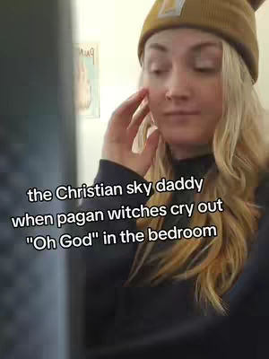 A woman wearing a beanie and a black top touches her face with her hand, a text overlay is present on the image