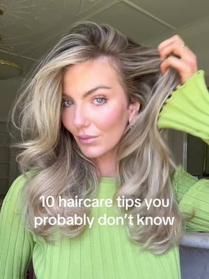 A woman with blonde hair styled in loose waves is holding a strand of hair, looking towards the camera. She is wearing a light green ribbed top and is set against a blurred background. Text overlayed on the image reads '10 haircare tips you probably don't know'.