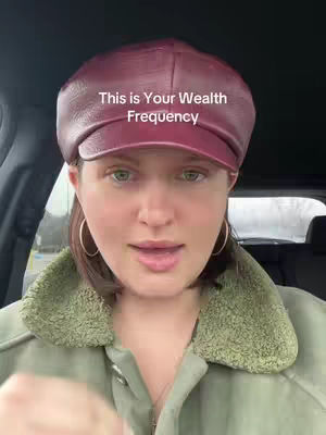 A woman in a burgundy hat and olive green jacket is seen from the chest up, with a text overlay at the top. The image has a neutral background, but it seems to be filmed inside of a car. The lighting appears to be daylight, highlighting the creator's face. The composition is centered, and the subject's expression is neutral.