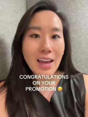 A woman with long dark hair and fair skin is centered in the frame. The background is a blurry, neutral gray. Text overlayed on the image reads, 'CONGRATULATIONS ON YOUR PROMOTION' with an emoji.