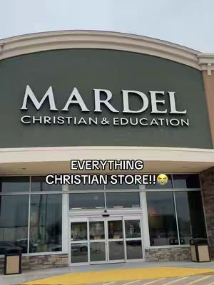 The storefront of a Mardel Christian & Education store is shown, with a gray-green facade and large glass windows, topped by a sign with the store's name in bold, white letters.