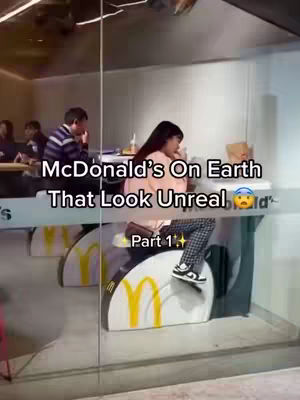 A person sitting on a McDonald's themed stool behind glass. The person is wearing black and white pants and black shoes. There is a McDonald's logo visible on the stool. The text overlay reads: McDonald's On Earth That Look Unreal.