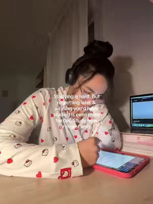 A person wearing headphones and pajamas is sitting at a wooden desk with a tablet and laptop. Text is overlaid, encouraging the viewer to choose between the pain of discipline or the pain of regret.