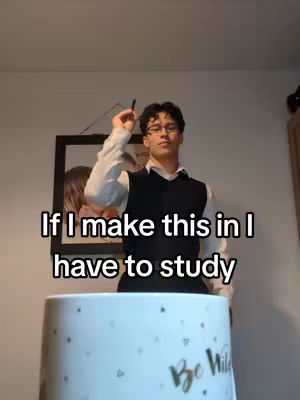 A young man is holding up a pen, the image is centered around him with a cup in the foreground.