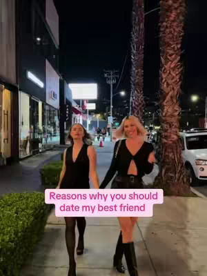 Two women walk side-by-side on a sidewalk at night. They are both dressed in black outfits. A pink banner across the bottom of the image reads 'Reasons why you should date my best friend'. The background includes buildings, streetlights, and a few people in the distance.