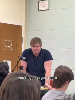 The image shows a man standing behind a podium, addressing a group of people. Text overlayed near the bottom says 'you're gonna get a zero'. The setting seems to be a classroom, possibly during an exam or academic dispute.