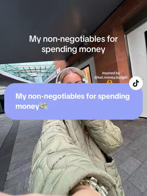 A selfie-style video cover image showing a person in a city setting. The person is wearing a light green quilted jacket and headphones. The main text overlay is a purple speech bubble with white text that reads "My non-negotiables for spending money 💸". A smaller text overlay at the top reads "My non-negotiables for spending money". The background is blurred but appears to be a commercial area with buildings and awnings.