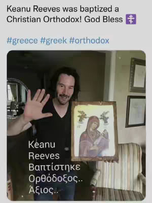 A candid photo of actor Keanu Reeves holding an Orthodox Christian icon and waving at the camera. The image is a screenshot, bearing text and hashtags related to Reeves' baptism and the Greek Orthodox faith. The image is in a home setting, featuring a chair and framed pictures in the background.