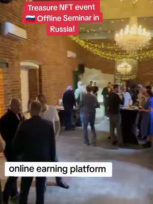 An indoor shot of a crowded event, likely a seminar or conference, with people in various outfits milling around. The room has a brick wall and a chandelier. There's text overlaid on the image. The event is about an online earning platform.
