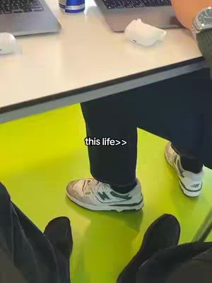 A person's legs and feet are shown from a low angle over a bright yellow-green surface. The person is wearing black pants and white sneakers with gray and green accents. The text overlay "this life>>" is positioned near the person's feet.
