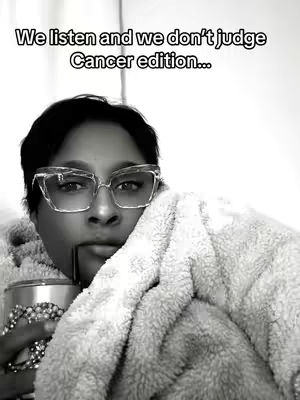 A black and white image of a person with dark hair and glasses, leaning against a fluffy blanket. The person holds a beverage in a metallic tumbler and gazes towards the camera. Text overlayed at the top reads: 'We listen and we don't judge Cancer edition...'