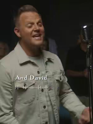 A man with short hair is singing into a microphone. The background is dark. Text overlayed on the image and appears to be a sound visualizer.