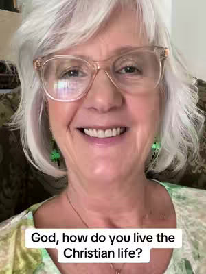 A close-up of a woman with short, silver hair, wearing clear-framed glasses and a light-colored top. She is smiling directly at the camera. A text overlay at the bottom reads, 'God, how do you live the Christian life?'