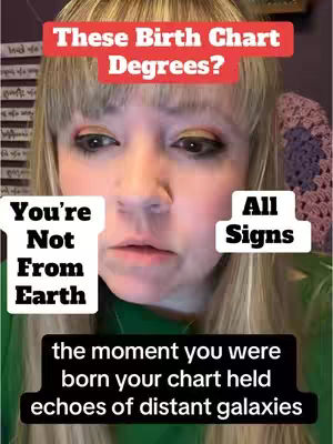 A close-up shot of a woman's face, with a soft focus. She has fair skin, blonde hair, and colorful eyeshadow. The background includes a wall with what appears to be patterned fabric and some text.