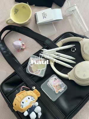 The image presents an overhead shot of a black tote bag, filled with various items. There is a yellow cup with a floral design. A small calendar with "2025" written on it. Clear cylindrical container. White pens, a pair of white headphones are seen in the background. Stickers are also on the bag. A Hello Kitty plushie is hanging from the bag. The overall aesthetic leans towards kawaii and desk organization, with a focus on cute stationery and accessories.