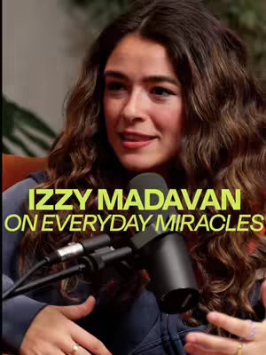 A woman with long, wavy brown hair is centered in the frame, looking slightly to the side and speaking. A microphone is positioned in front of her. Text overlayed on the image in a vibrant yellow capitalizes her name and the video topic.