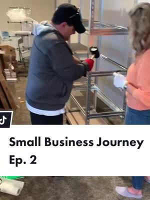The image shows a man in a grey hoodie and black cap hammering metal shelves, with a woman in the background. Text overlayed at the bottom says 'Small Business Journey Ep. 2'.