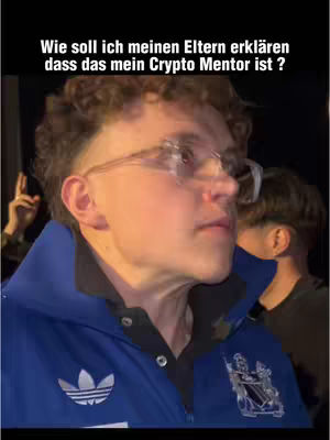 A young man with short, styled hair and glasses is the central focus, looking slightly off-center. He wears a blue and black Adidas jacket, with a blurred background suggesting an indoor setting. The Adidas logo is visible on the jacket. The text overlay states 'Wie soll ich meinen Eltern erklären dass das mein Crypto Mentor ist ?' (How should I explain to my parents that this is my Crypto Mentor?).