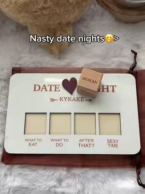 A white board with four rectangular cutouts displays phrases like 'What to Eat' and 'Sexy Time', overlaid on a fuzzy, light-colored surface. Above the board, text reads 'Nasty date nights.' A small wooden cube labeled 'Mexican' sits near a heart symbol. The overall composition suggests a fun, relationship-oriented theme.