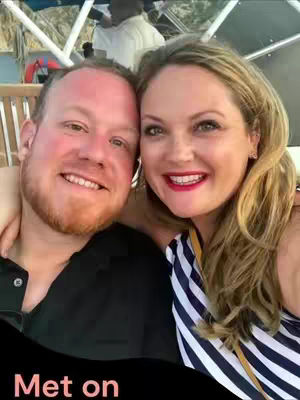 A selfie-style photo of a smiling couple, the man on the left has red hair and a partial beard, and the woman on the right has blonde hair and is smiling, the couple is embracing and it looks like the photo was taken on a boat or outdoor setting.