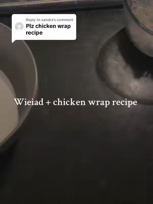 The image shows a top-down view of a dark surface, likely a countertop. Two white bowls partially visible on the sides. In the center, white text overlays read 'Wieiad + chicken wrap recipe'. A comment bubble in the top left states 'reply to Sandra's comment Plz chicken wrap recipe'