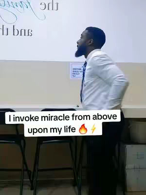 The image features a man in a white shirt, standing next to a table with his back to the camera, looking upwards. Text overlay at the bottom reads, \"I invoke miracle from above upon my life\" with a flame and lightning bolt emoji.