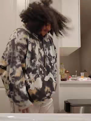 The cover image shows a person with long, dark, slightly wavy hair, wearing a light-colored tie-dye hoodie. The person has their head tilted back, and their hair is moving as if they are dancing or shaking their head. The background shows a kitchen with white cabinets and a counter. The lighting is bright, and it appears to be indoors.