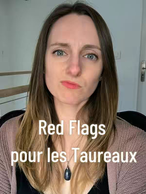 A woman with light brown hair and blue eyes is in a close-up shot, with a slightly surprised expression. The words "Red Flags pour les Taureaux" are written as the video hook in a white sans-serif font, centered and in bold. She wears a pink cardigan over a dark top, and a necklace with a black teardrop-shaped pendant.