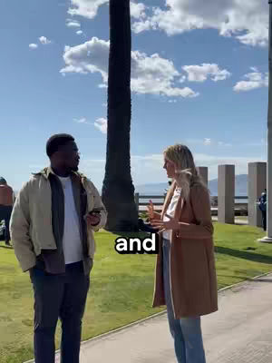 Two people are standing and talking outside, with a large tree trunk in the background. The sky is blue with clouds. There is text overlayed on the image.